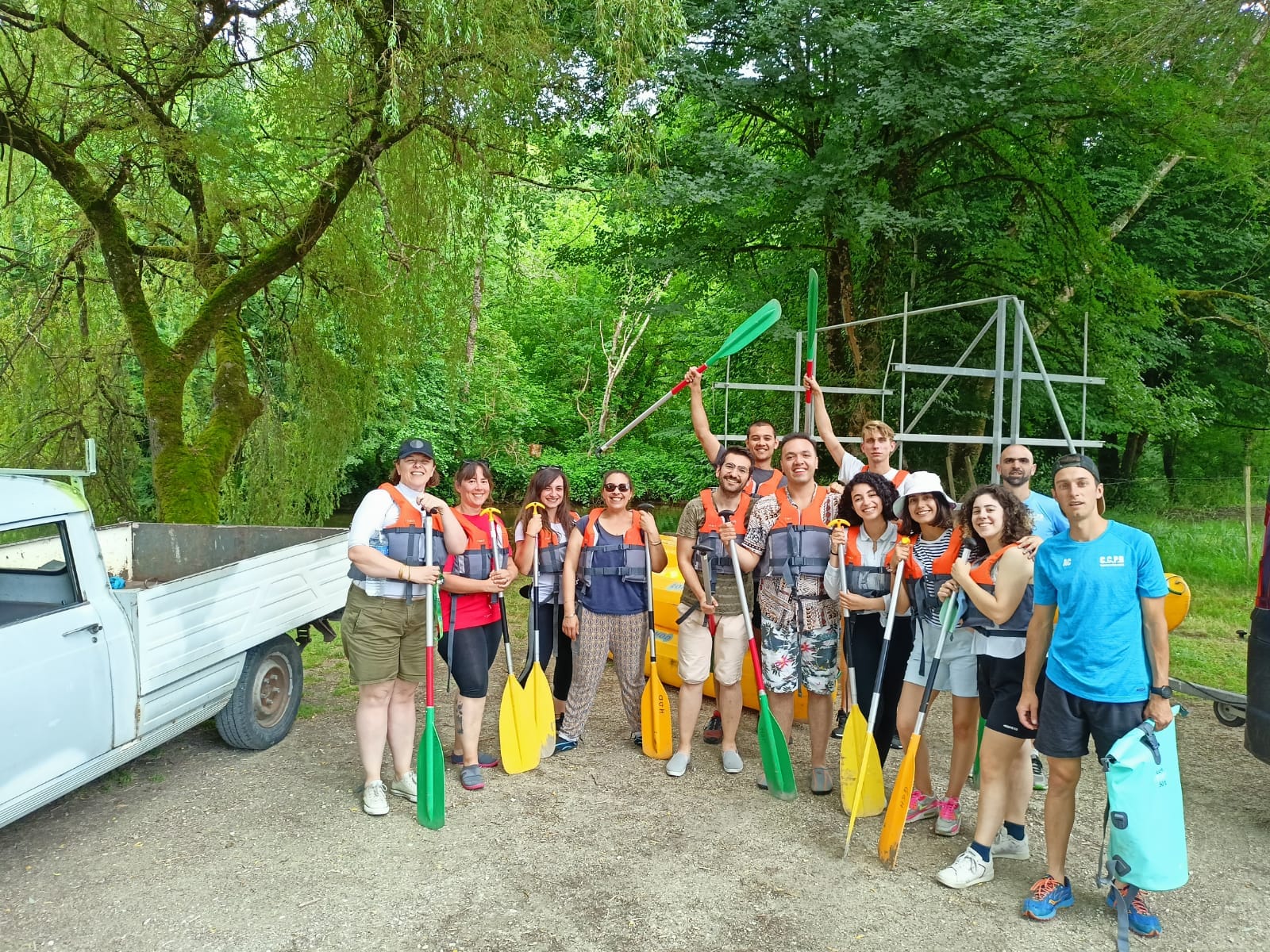 Gruppo di volontari sorridenti pronti per un'attività all'aperto con pagaie, circondati dalla natura.