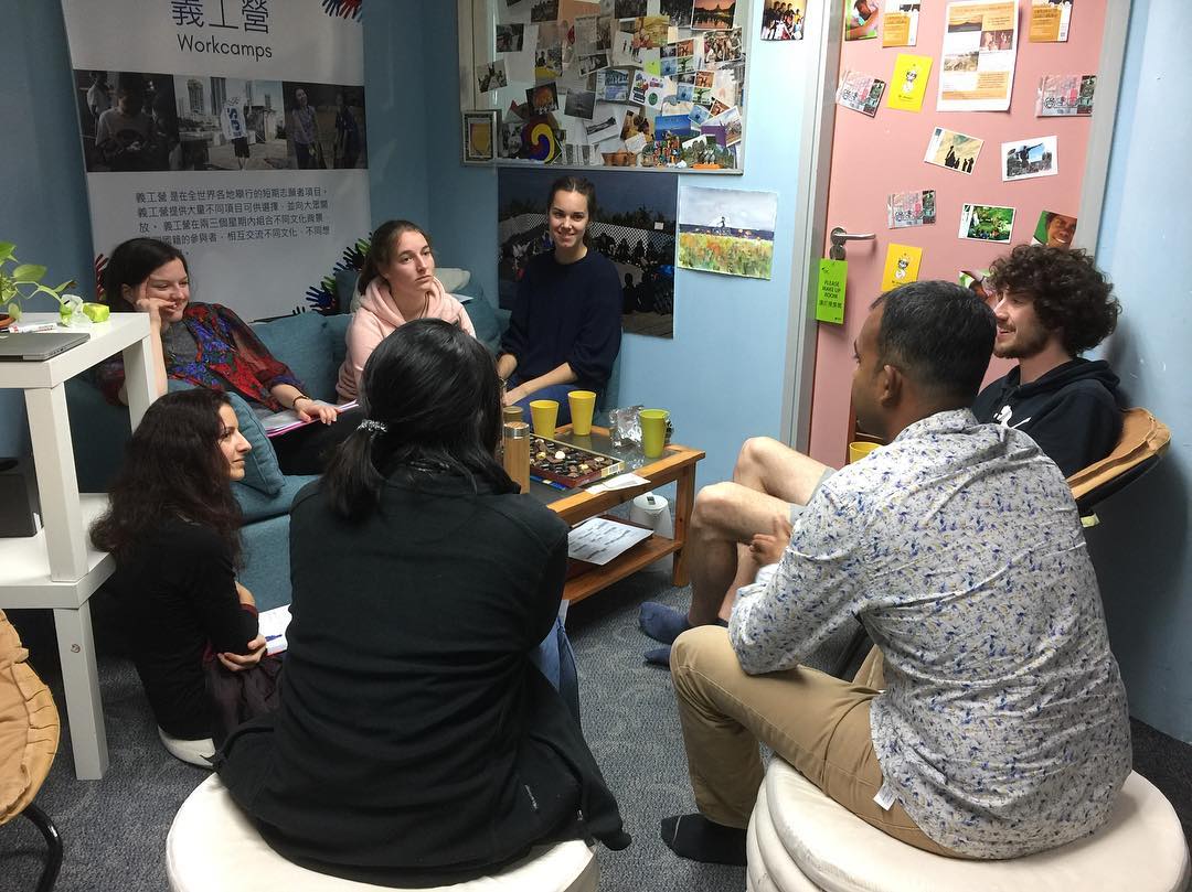 Un gruppo di persone sedute in cerchio in una stanza decorata con foto e poster.