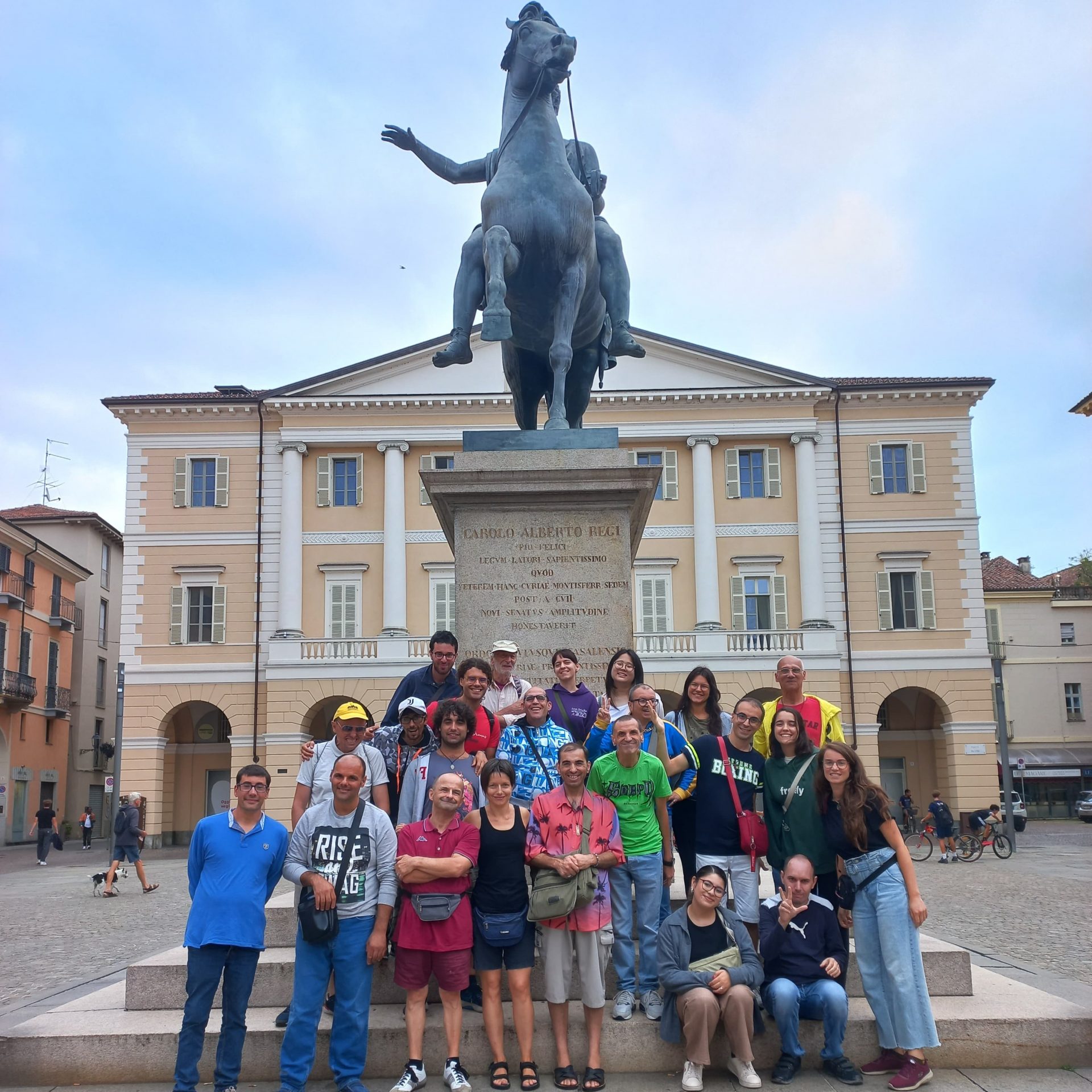 Gruppo di persone in posa davanti a una statua equestre in piazza.